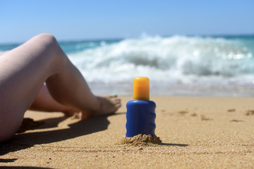 Close-up on female legs and sunscreen cream sand. Concept of skin care and sunbathing