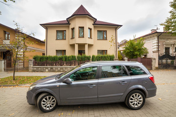 New expensive gray car parked in paved parking lot in front of big two story cottage. Luxury and...