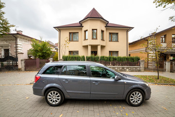 Fototapeta na wymiar New expensive gray car parked in paved parking lot in front of big two story cottage. Luxury and prosperity concept.