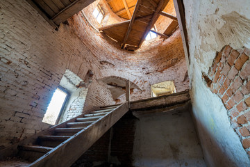 Large spacious forsaken empty basement room of ancient building or palace with cracked plastered brick walls, small windows, dirty floor and wooden staircase ladder.