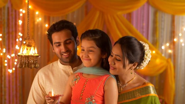Nuclear Indian family portrait : Little daughter lighting diyas. Complete Family in India. Indian stock video of a happy nuclear family celebrating Diwali together by lighting their house with diya