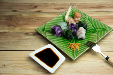 Various of steamed chive dumplings with dry garlic served on green leaf ceramic square plate on bright wood table background.