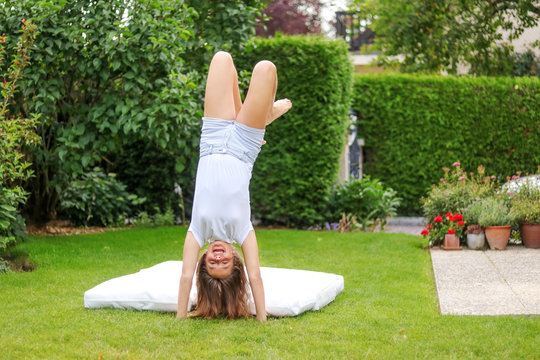 Funny preteen girl doing handstand on grass having fun in the garden outdoors at summer day at green hedge background. Summer holidays lifestyle. Child activity