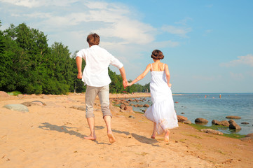 young loving couple in white running on the sand near the sea