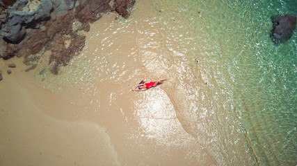 Pretty woman in red bikini swimsuit enjoys water of sea, brown sand. Birds eye view taken by a drone. Aerial photo - Powered by Adobe