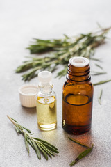 Rosemary essential oil in a glass bottle with fresh branch rosemary herb on grey table for spa,aromatherapy and bodycare.Copy space.