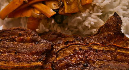 Crispy dark brown roasted pork belly seasoned with coarse ground pepper, on white rice with carrot sticks