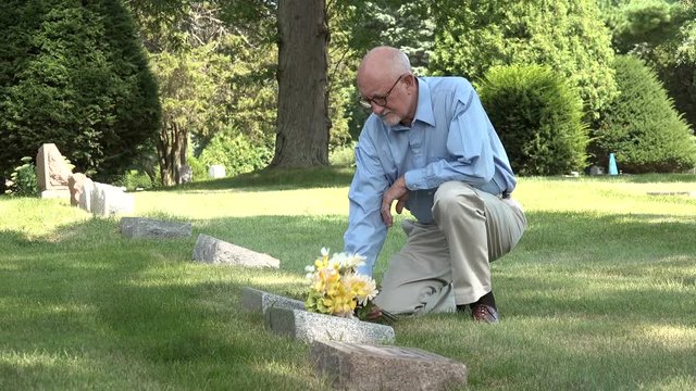Man kneeling at grave with flowers