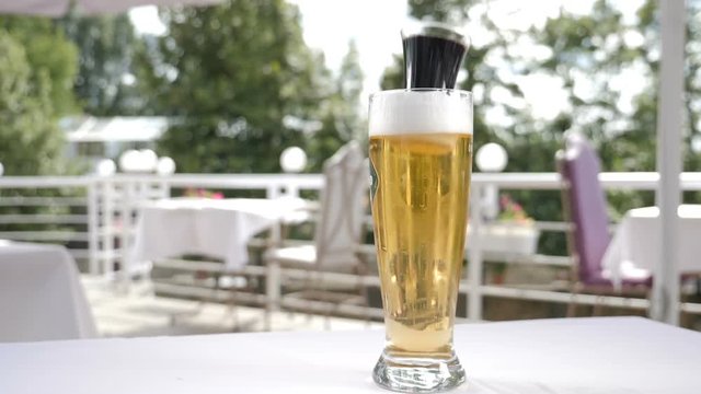 Beer splashing. Beer beverage serving. Small flass with dark alcoholic liquid falling into glass with beer. Slow motion. Splashes with overflow frothy foam. hd