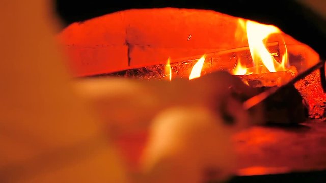 Backer is preparing wood and fire in a traditional old oven with natural firewood, coal and flame is ready for backing pizza. Red, orange colors