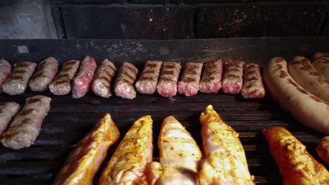 Mixed juicy tasty meat roasting on hot charcoal fired barbecue mesh closeup. Filmed while grilling sausages and chicken kebabs with some minced meat cevapcici.