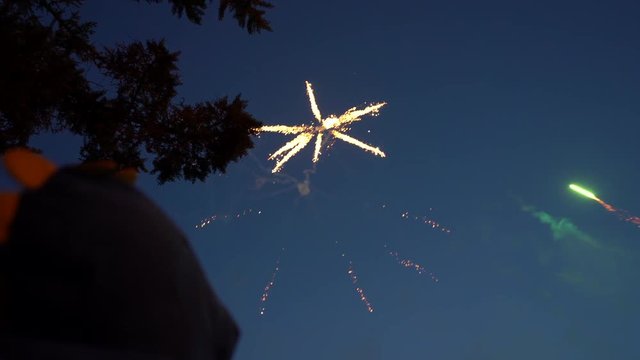 The child in the hood looks at the blue sky, the night sky appears volleys of fireworks orange. Fireworks