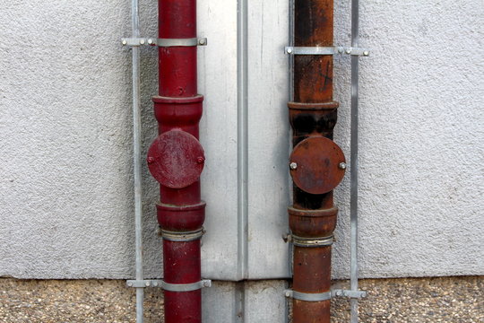 Two strong rusted metal gutter rainfall pipes connected to lightning rod on both sides mounted on side of local apartment building on warm sunny spring day