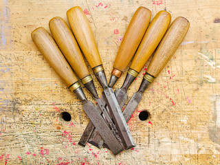 Group of assorted woodworking chisels isolated on wooden bench grunge surface.