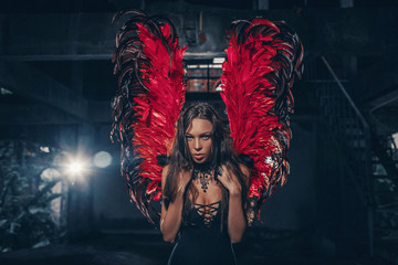 Art photo of an Dark Angel beautiful woman. A girl with red devil wings and a black dress in the...