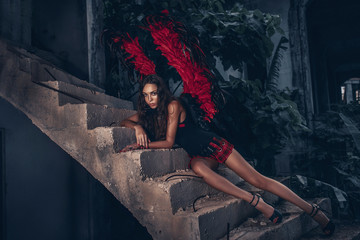 Temptress concept. Woman on passionate face play role game. Girl sexy demon in  black dress with red wings, devil full of desire lying  on the stairs