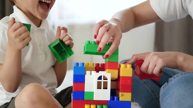 Close-up of the house from meccano. A woman and a little boy build a house of colored blocks, experiencing emotions of happiness and laughter.