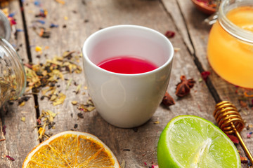 cups of healthy herbal tea with cinnamon, dried rose and camomile flowers in spoons over wooden...