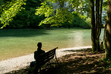woman enjoys sitting on a bench under shady trees on an idyllic river bank