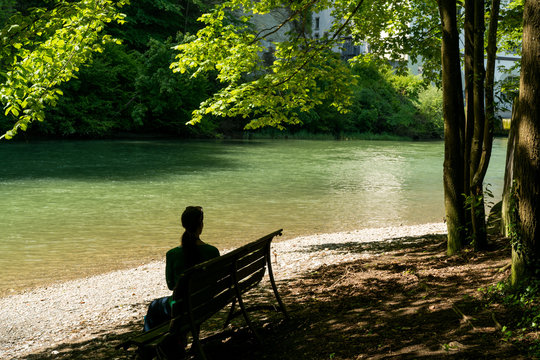 woman enjoys sitting on a bench under shady trees on an idyllic river bank