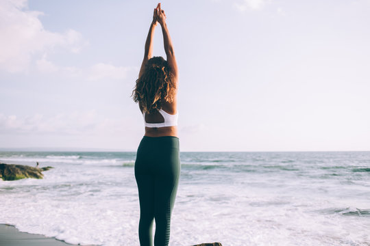 Back view of young woman doing tadasana for relaxes centers attention and sharpens concentration, female enjoying time for practising yoga on coastline training balance and harmony on nature