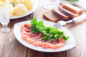 Homemade red salted fish on a white bowl on a background of boiled potatoes, horizontal