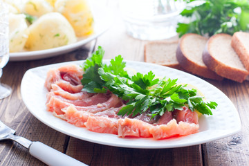 Homemade red salted fish on a white bowl on a background of boiled potatoes, horizontal