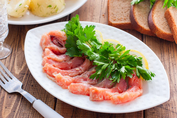 Homemade red salted fish on a white bowl on a background of boiled potatoes, horizontal