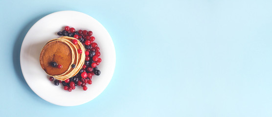 A stack of pancakes with blueberries and cranberries on a white plate.