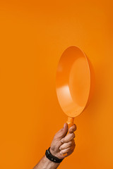 Colored pan in the hand. A hand is holding a orange pan on a colored background. Colored pan isolated. Cooking food concepts