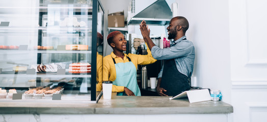 Excited black baristas doing high five in cafe