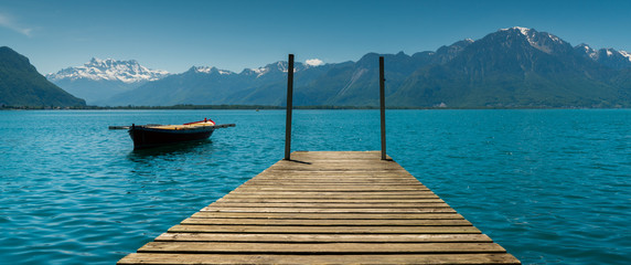 mountain and lake landscape with a vintage rescue rowboat and a wooden pier - obrazy, fototapety, plakaty