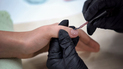 Manicure master applying nude gel nail polish, beauty salon procedure, hygiene