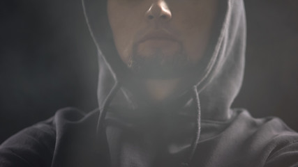 Man in hoodie sitting in dark room full of smoke, anonymous hacker, criminal