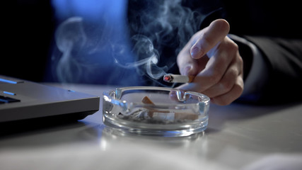 Female hand throwing cigarette ash in tray, smoking at workplace, stressful job