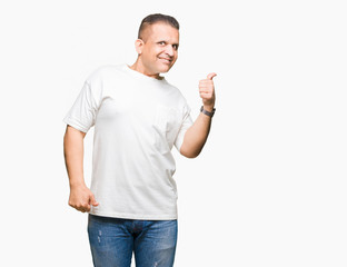 Middle age arab man wearig white t-shirt over isolated background smiling with happy face looking and pointing to the side with thumb up.