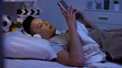 Cute teenager listening music in headphones and scrolling smartphone, relaxation