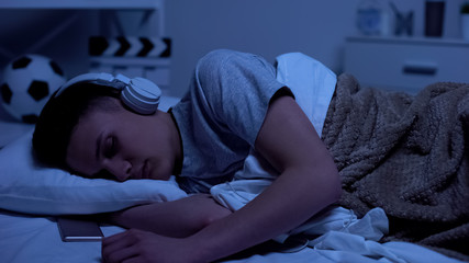 Male teenage boy fallen asleep in headphones, overworked student relaxing