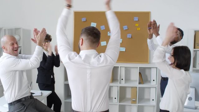 Three-shot sequence of man throwing darts at pin board with motivational goals, colleagues cheering with hands in air, with cut-in of dart hitting word &ldquo;boss&rdquo;, and man collecting darts to start again