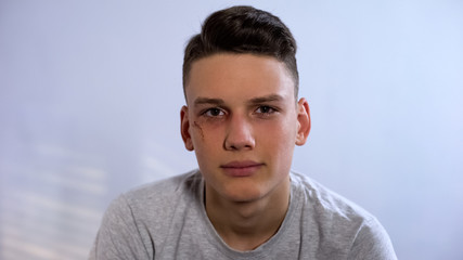 Upset male teenager with wounded face looking at camera, assault in family