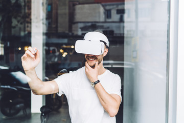 Cheerful hipster guy in electronic goggles working in cyberspace using high technology for testing...