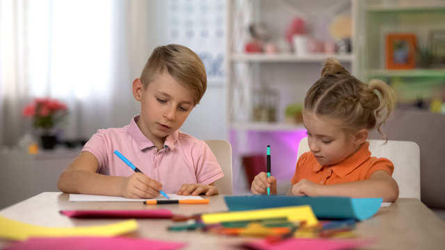 Adorable boy and girl drawing with pencils, sitting at table, kindergarten