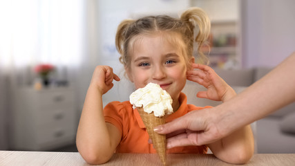 Cute girl tasting ice-cream cone from female hand, childhood surprise, snack