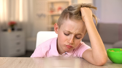 Sad boy sitting at kitchen table, refusing to eat healthy but tasteless meal
