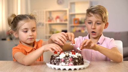 Brother and sister taking cherries from top of delicious cream cake, celebration