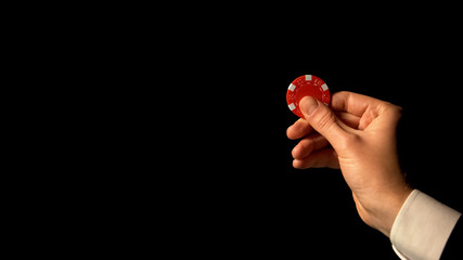 Hand in suit showing red chip against black background, successful poker bets