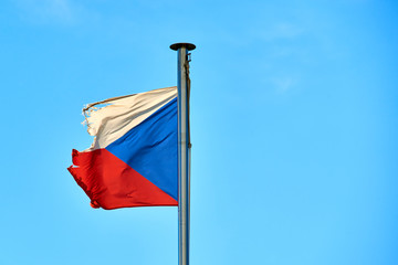 Tattered Czech Republic flag against blue sky blowing in the wind with copy space