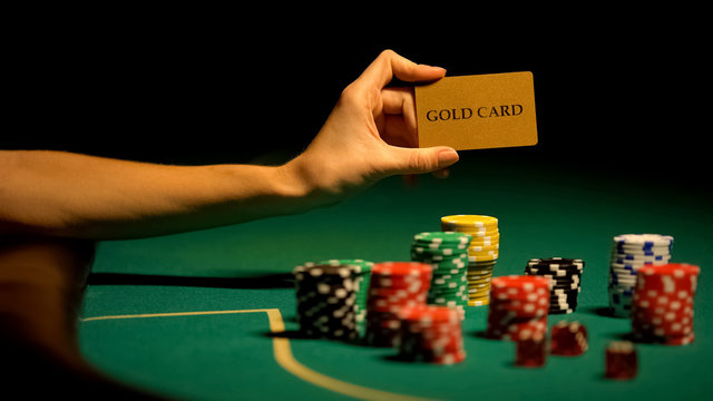 Hand holding gold card, gambling chips on table, illegal casino for VIP-clients