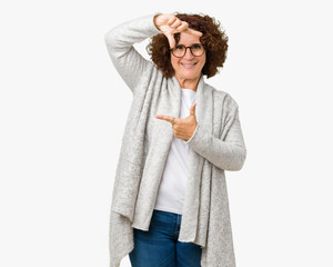 Beautiful middle ager senior woman wearing jacket and glasses over isolated background smiling making frame with hands and fingers with happy face. Creativity and photography concept.