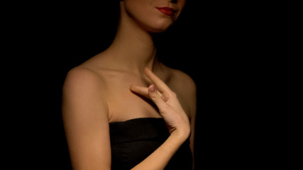 Flirty woman stroking her body isolated on dark background, prostitution concept